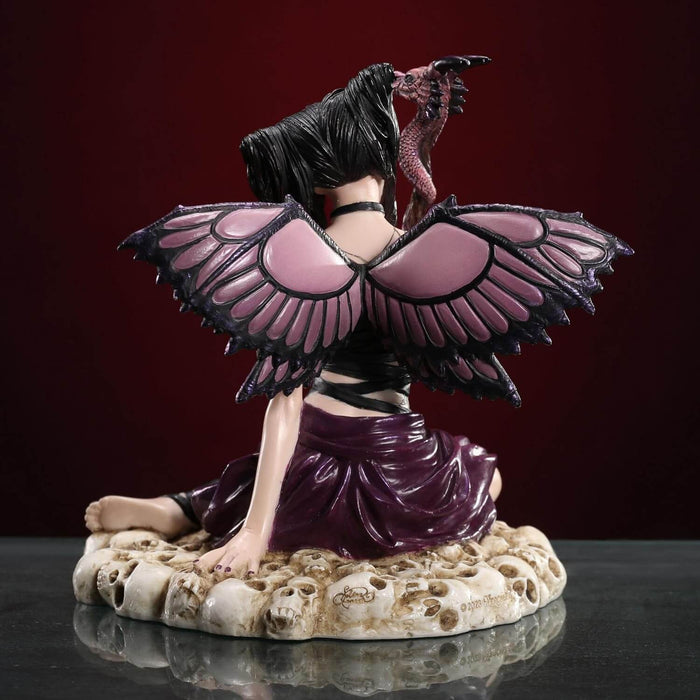 Fairy figurine of pixie with purple and black wings and outfit holding a dragon staff and sitting on skulls. Shown from the back