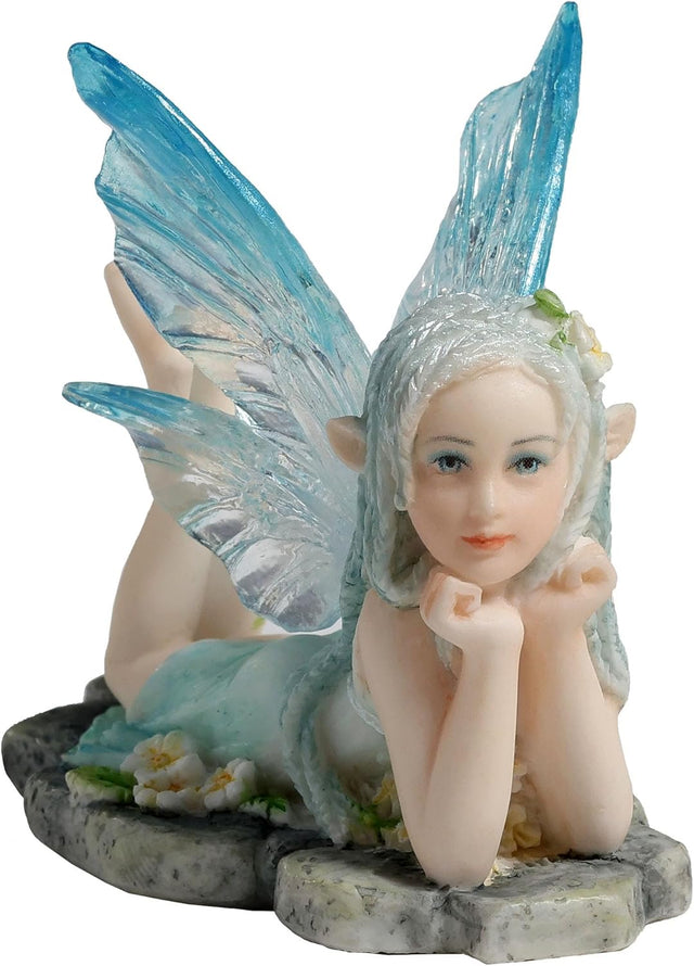 Figurine of fairy in pale blue dress with clear and blue wings and braided hair lying amidst flowers on a stone, feet kicked up