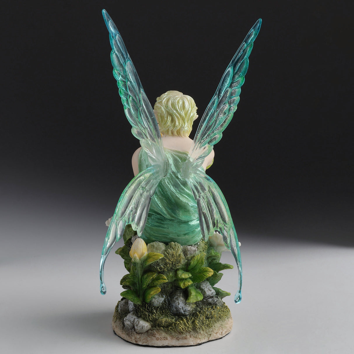 Fairy figurine with green wings, sitting on a base with plants and rocks, shown from the back