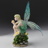 Fairy figurine with green toga and aqua wings sitting on a rock with flowers.