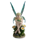 Fairy figurine with green wings sitting among flowers on a white background