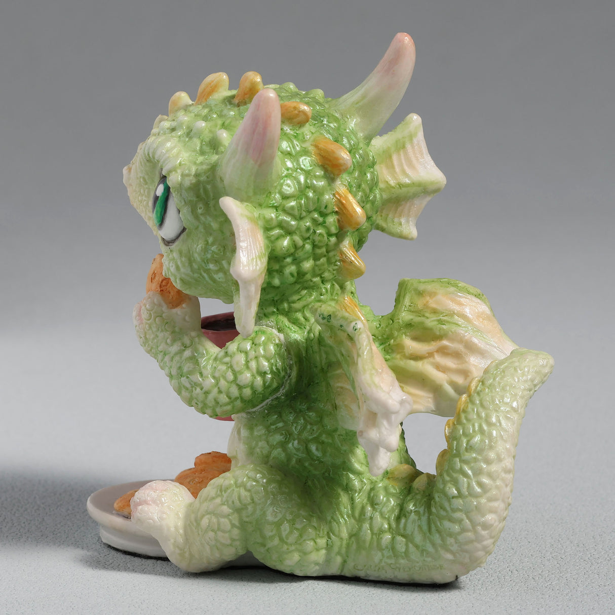 Figurine of a green baby dragon with a pink heart mug and plate of cookies