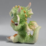 Figurine of a green baby dragon with a pink heart mug and plate of cookies