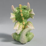 Figurine of a green baby dragon with a pink heart mug and plate of cookies. Shown from the back