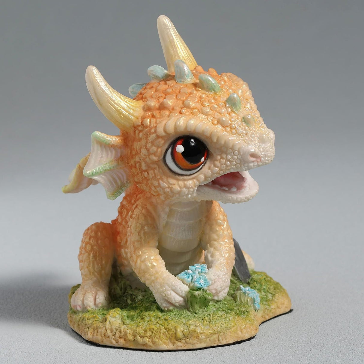 Figurine of a pale gold baby dragon gardening with flowers and a trowel