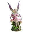 Fairy figurine with purple wings and pink dress sitting amidst clover flowers