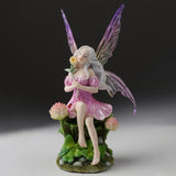Fairy figurine with purple wings and pink dress sitting amidst clover flowers