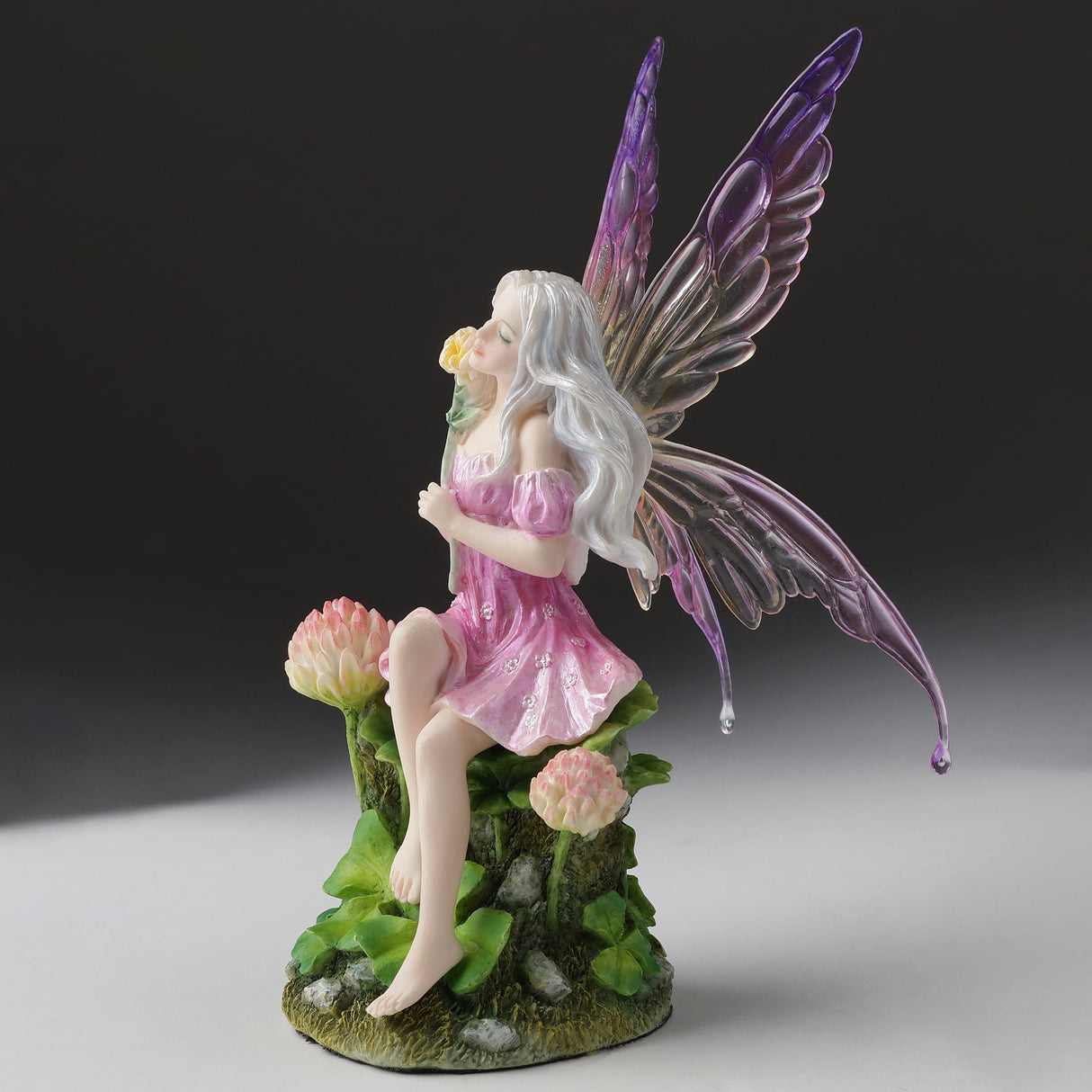 Fairy figurine with purple wings and pink dress sitting amidst clover flowers