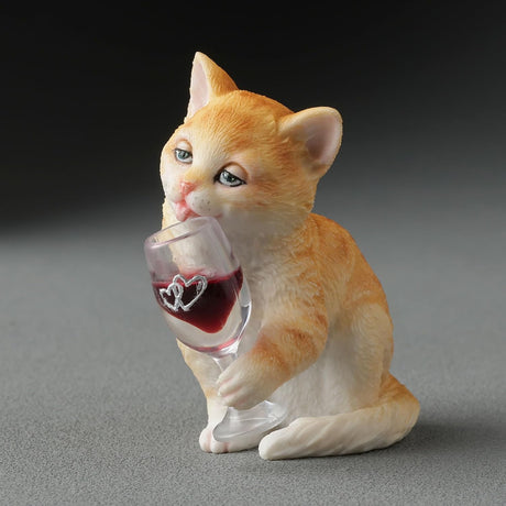 Orange cat figurine holding a wine glass with red wine