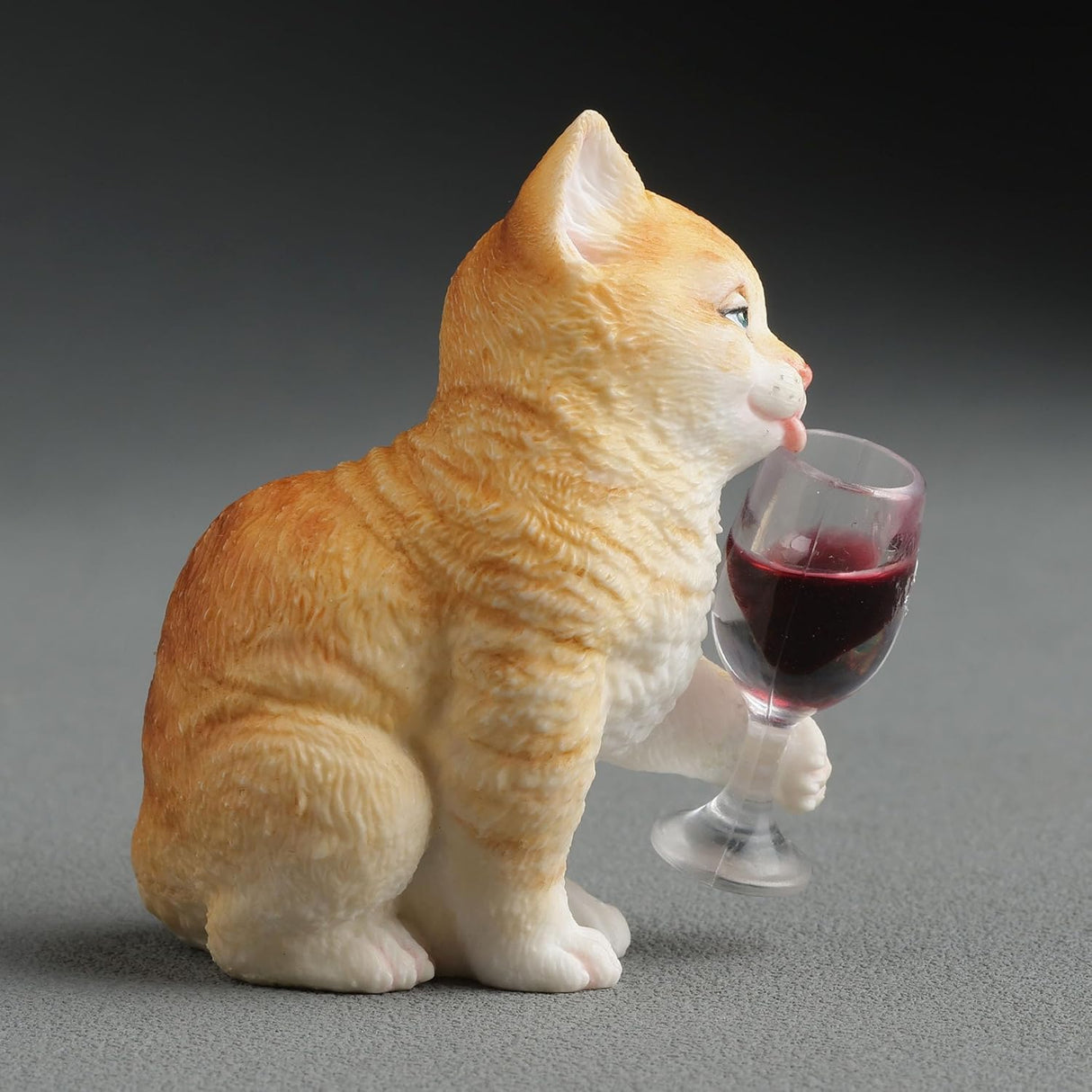 Orange cat figurine holding a wine glass with red wine