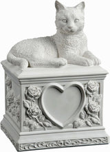 A white cat cremation urn featuring a detailed cat figurine resting on a square pedestal decorated with a central heart-shaped recess and embossed floral rose motifs.