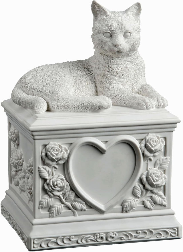 A white cat cremation urn featuring a detailed cat figurine resting on a square pedestal decorated with a central heart-shaped recess and embossed floral rose motifs.