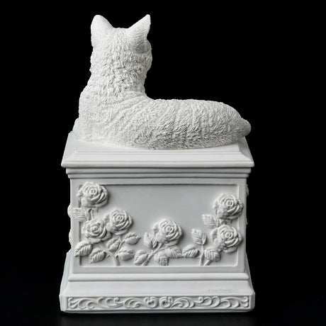 A white cat cremation urn featuring a detailed cat figurine resting on a square pedestal decorated with a central heart-shaped recess and embossed floral rose motifs. Shown from the back