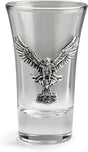 A clear glass shot glass featuring a detailed, raised pewter hawk emblem holding a hammer on the front