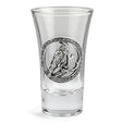 A clear glass shot glass featuring a detailed pewter raven emblem in the center