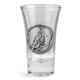 A clear glass shot glass featuring a detailed pewter raven emblem in the center