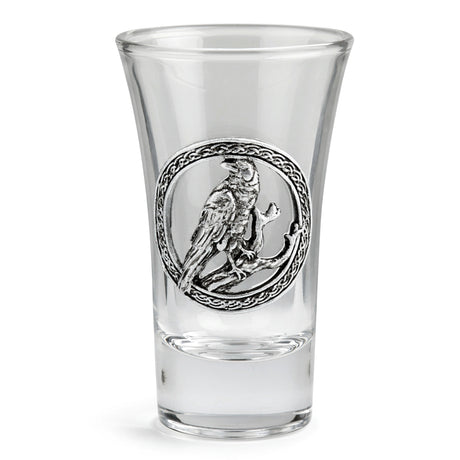 A clear glass shot glass featuring a detailed pewter raven emblem in the center