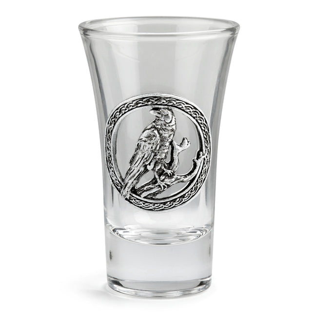 A clear glass shot glass featuring a detailed pewter raven emblem in the center