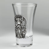 A clear glass shot glass featuring a detailed pewter relief of a triple moon goddess figure, Hecate, flanked by two wolves