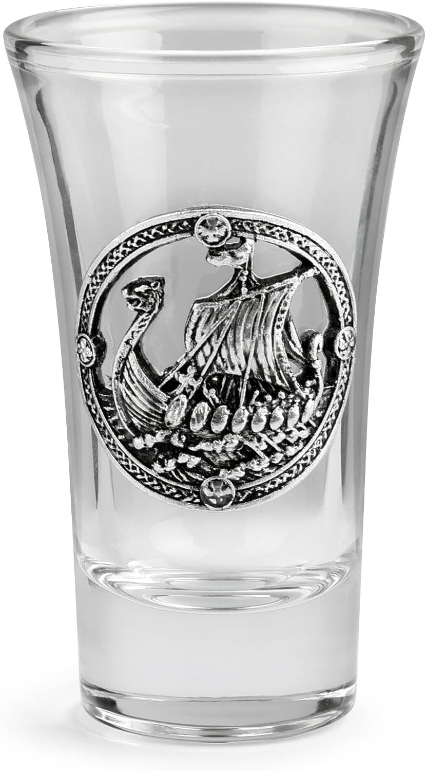 A clear glass shot glass featuring a pewter Viking ship medallion on the front