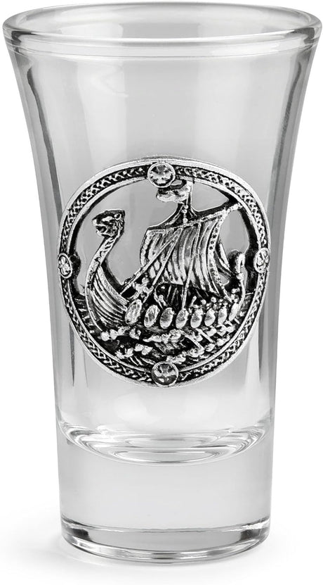 A clear glass shot glass featuring a pewter Viking ship medallion on the front