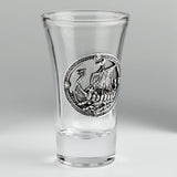 A clear glass shot glass featuring a pewter Viking ship medallion on the front