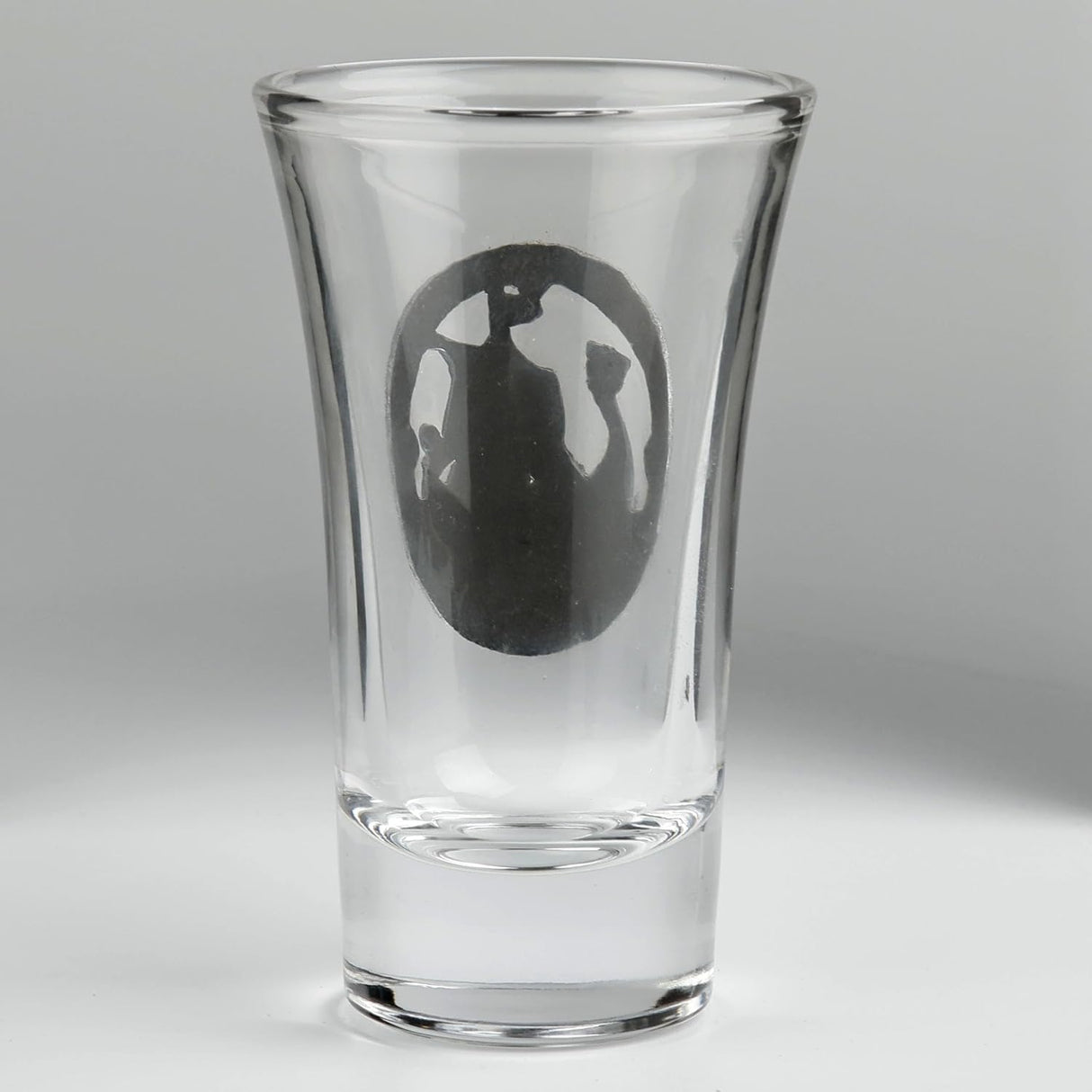 A clear glass shot glass featuring a pewter Viking ship medallion on the front. Shown from the back