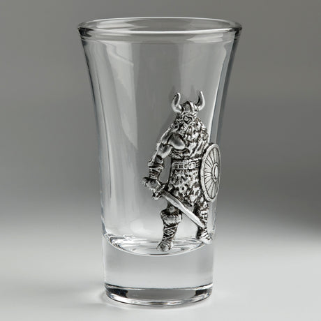 A clear glass shot glass featuring an embossed pewter Viking warrior holding a shield and sword