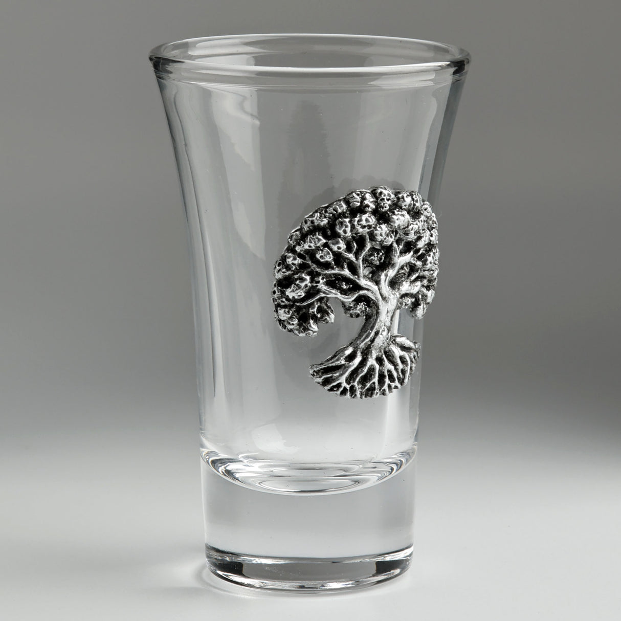 A clear glass shot glass featuring a detailed pewter tree of life emblem