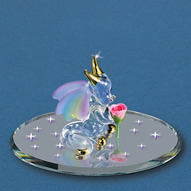 Glass figurine of a baby dragon with rainbow wings on a round base with rose, against a blue background