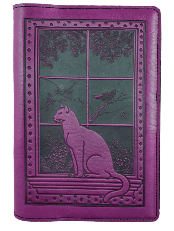 Leather notebook cover showing a cat sitting on a windowsill with birds, tree, flowers beyond. Shown in orchid purple.