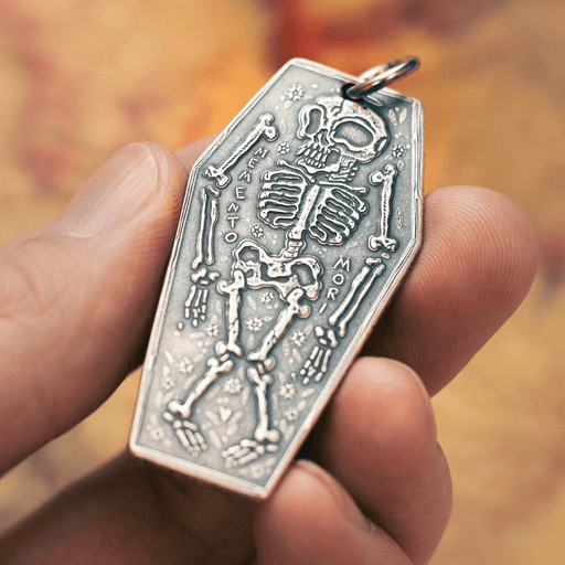 Silver charm featuring a skeleton and the phrase "Memento Mori"