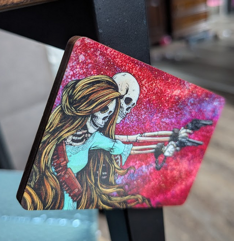 Magnet with a skeleton couple, each holding a gun against a colorful background