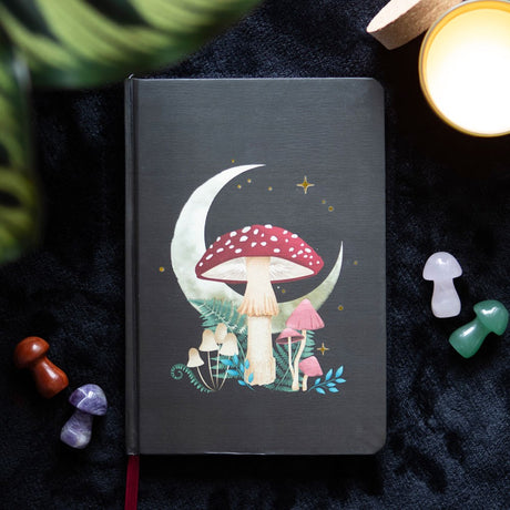 Black journal with moon and mushroom cover art, red ribbon bookmark