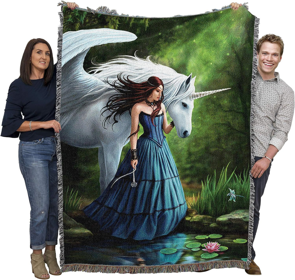 A large woven throw blanket featuring an illustration of a woman in a blue gown standing in a pond beside a white unicorn, held up by two people against a plain white background.