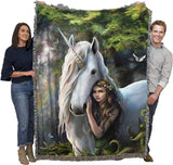Blanket with a design of a woman hugging a unicorn in a forest setting, held by two people.