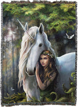 Blanket with a design of a woman hugging a unicorn in a forest setting