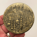 Back of coin held in a hand showing treasure and chest in cave with skulls
