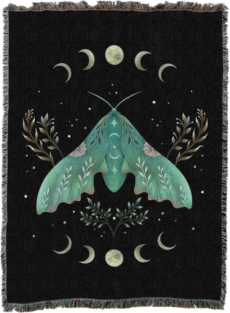 A black woven throw blanket with fringe edges, featuring a large teal-green moth surrounded by cream-colored crescent moons, stars, and botanical motifs.