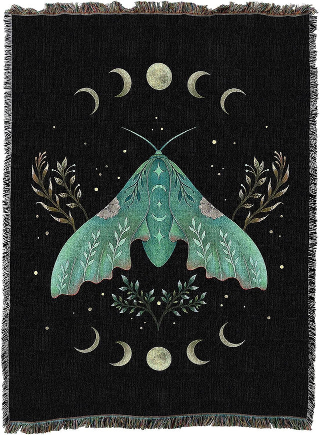 A black woven throw blanket with fringe edges, featuring a large teal-green moth surrounded by cream-colored crescent moons, stars, and botanical motifs.