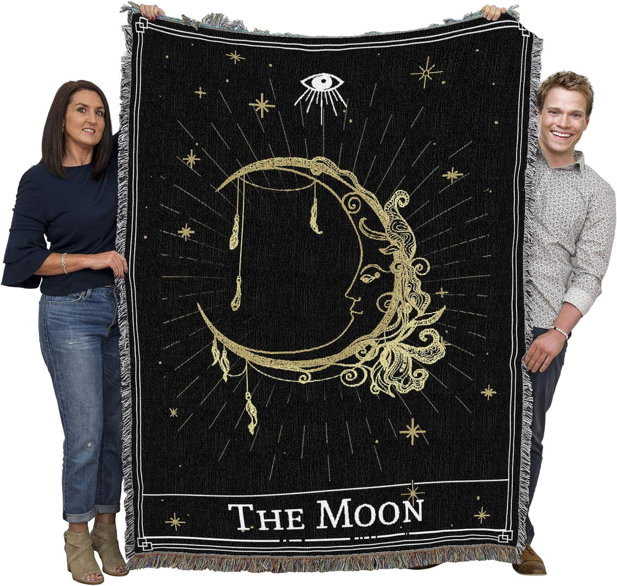 Two people holding a black and gold 'The Moon' tapestry with celestial designs.