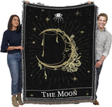 Two people holding a black and gold 'The Moon' tapestry with celestial designs.