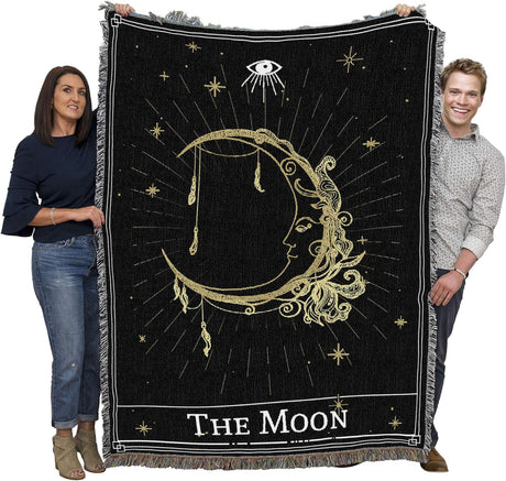 Two people holding a black and gold 'The Moon' tapestry with celestial designs.