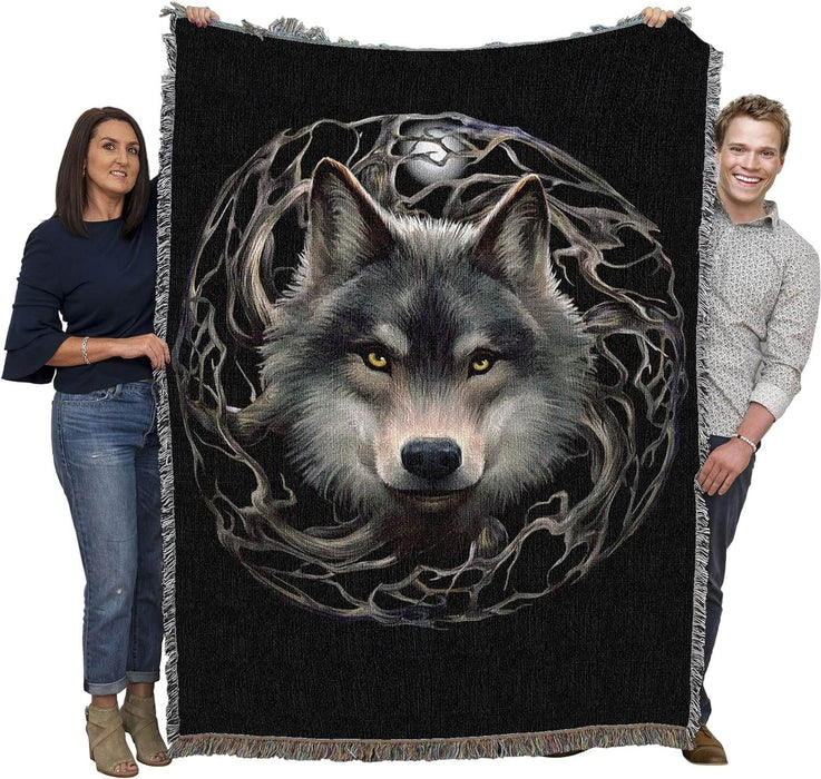 Tapestry blanket with background in black, showing wolf face at the center of a circle of tree branches with a full moon, shown held by adults