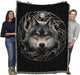 Tapestry blanket with background in black, showing wolf face at the center of a circle of tree branches with a full moon, shown held by adults