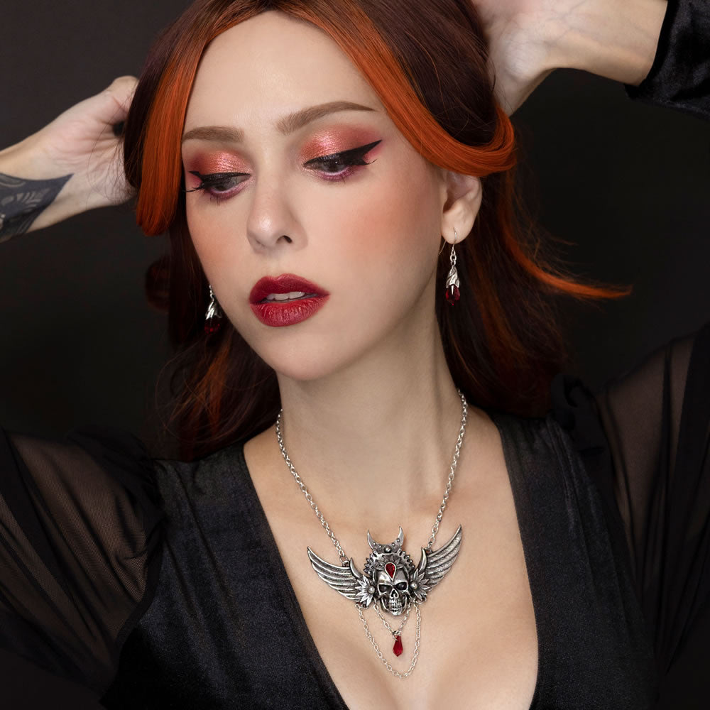 Woman with red hair and dark makeup wearing a necklace with a prominent skull pendant.