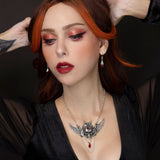 Woman with red hair and dark makeup wearing a necklace with a prominent skull pendant.