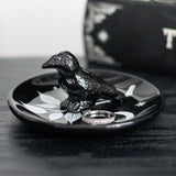 Black ceramic dish with a raven bird design, leaves and moon, shown with ring