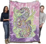 Two people holding a colorful tapestry with a seahorse design against a pink and purple patterned background.