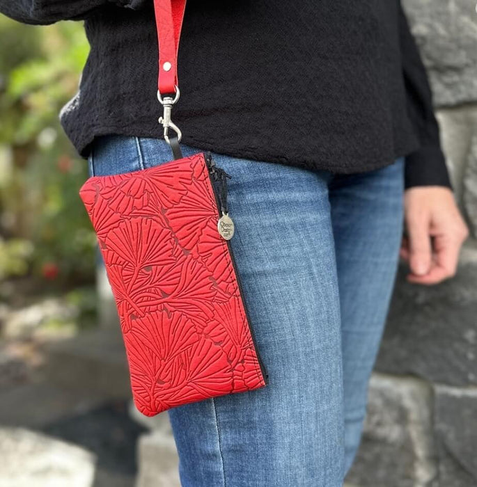 Ginkgo leaves on a leather wristlet pouch, shown in red held by a woman in jeans